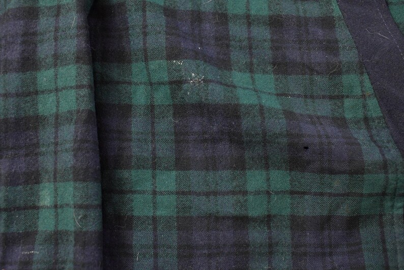 Puede incluir: Primer plano de una secci&oacute;n de tela con un patr&oacute;n de cuadros cl&aacute;sico. El dise&ntilde;o presenta una cuadr&iacute;cula de l&iacute;neas que se cruzan en tonos de verde y azul marino. La tela tiene un aspecto ligeramente texturizado.