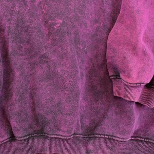 May include: A long-sleeve sweatshirt featuring a deep magenta and black acid-wash pattern. The garment includes a ribbed crew neckline, ribbed cuffs at the end of the sleeves, and a ribbed hemline along the bottom edge, showcasing a textured finish.