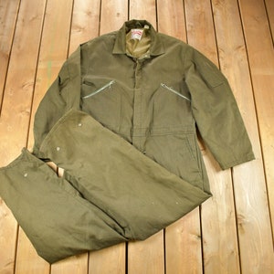 Puede incluir: Un mono de trabajo verde con cremallera frontal y múltiples bolsillos. El mono está hecho de un tejido resistente y tiene un corte holgado.