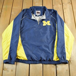 May include: Navy blue and yellow athletic jacket with a half-zip closure. The jacket features a yellow "M" logo on the chest and yellow side panels. The jacket has a stand-up collar and elastic cuffs and hem.