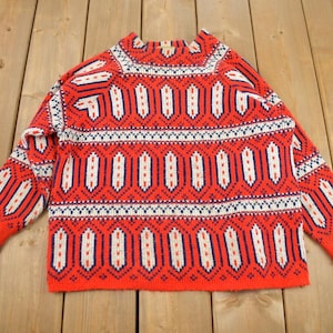 Pode incluir: Um suéter vermelho, branco e azul com gola redonda.