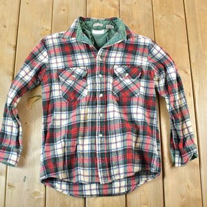 May include: A long-sleeved plaid shirt in red, white, and navy blue with a green collar and lining. The shirt has two chest pockets and white buttons down the front. The fabric appears to be a soft flannel.