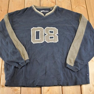 May include: Navy blue long-sleeve shirt with the number "08" in a white and gray design on the front. The shirt has a V-neck collar and gray accents on the sleeves.