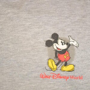 Op de afbeelding: Grijze sweatshirt met ritssluiting met een Mickey Mouse-afbeelding. Het stripfiguur is afgebeeld in zijn klassieke outfit met rode shorts en gele schoenen. De woorden "Walt Disney World" zijn in het rood gedrukt.