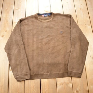 May include: A brown jumper with a small logo on the chest. The jumper is made of a soft, textured fabric.