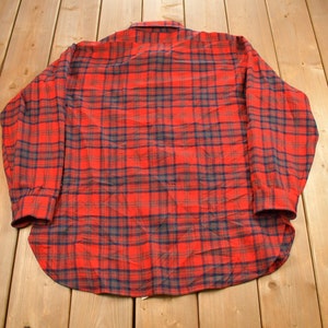 Puede incluir: Una camisa de franela a cuadros rojos y azules con mangas largas y cierre de botones.