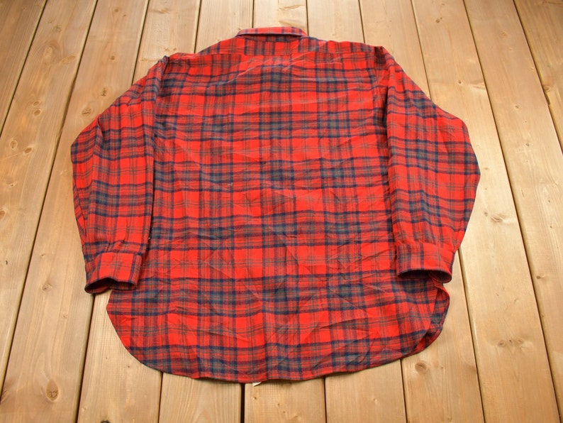 Puede incluir: Una camisa de franela a cuadros rojos y azules con mangas largas y cierre de botones.