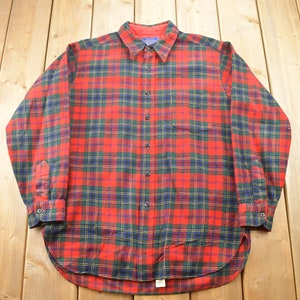 May include: A red, green, and blue plaid flannel shirt with long sleeves and a button-up front.