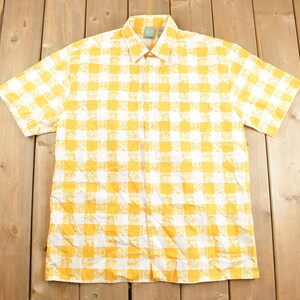 May include: A yellow and white checkered short-sleeved button-up shirt. The shirt has a white background with a yellow checkered pattern.