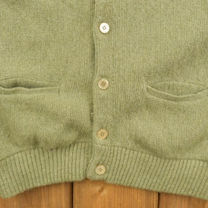 May include: A green knitted cardigan with a button-up front and two pockets. The cardigan has a ribbed hem and cuffs.
