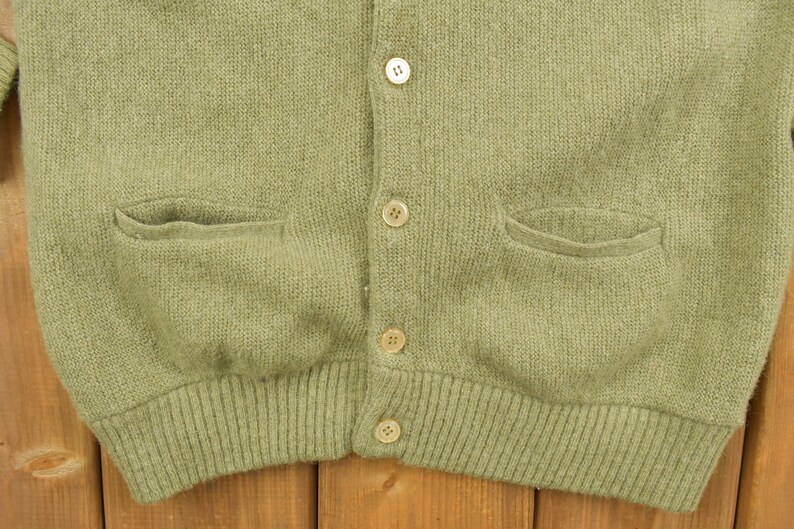 May include: A green knitted cardigan with a button-up front and two pockets. The cardigan has a ribbed hem and cuffs.