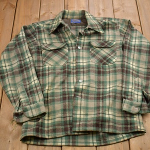 May include: A green, brown and white plaid flannel shirt with long sleeves and a button-up front.