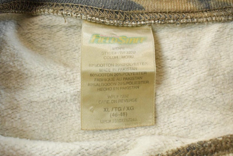 May include: A close-up of a clothing label, tan in colour, with black text. The label reads "MENNS", "STYLE: WF3200", and "COLOR: MOBU". It details the fabric composition as 80% cotton and 20% polyester. The size is XL/TG/XG (46-48).
