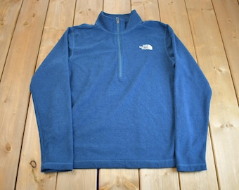 May include: A blue fleece pullover with a quarter zip and the North Face logo on the chest.
