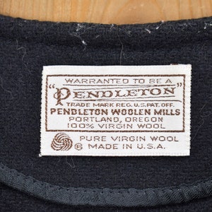 K&ouml;nnte beinhalten: Nahaufnahme eines schwarzen Stoffes mit einer gen&auml;hten Kante und einem rechteckigen Etikett. Das Etikett lautet "PENDLETON WOOLEN MILLS, PORTLAND, OREGON, 100% VIRGIN WOOL, PURE VIRGIN WOOL, MADE IN U.S.A."