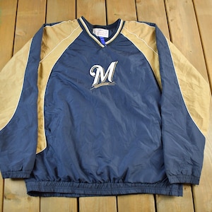 Könnte beinhalten: Marineblaue und beige Pulloverjacke mit dem Buchstaben "M" auf der Brust gestickt. Die Jacke hat einen V-Ausschnitt und elastische Bündchen und Saum. Die Ärmel und Schultern sind beige, und der Körper ist marineblau.