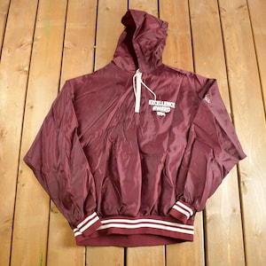 May include: A maroon hooded windbreaker with white stripes on the cuffs and waistband. The jacket has a zipper closure and a drawstring hood. The front of the jacket features a white embroidered logo that reads "Excellence Award 1994".