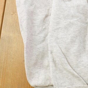 Op de afbeelding: Een lichtgrijs sweatshirt met een gespikkelde of gem&ecirc;leerde textuur door de hele stof. Het kledingstuk heeft een zacht, gevouwen uiterlijk met zichtbare kreukels en een consistent lichtgrijs kleurenpalet over het gehele oppervlak.