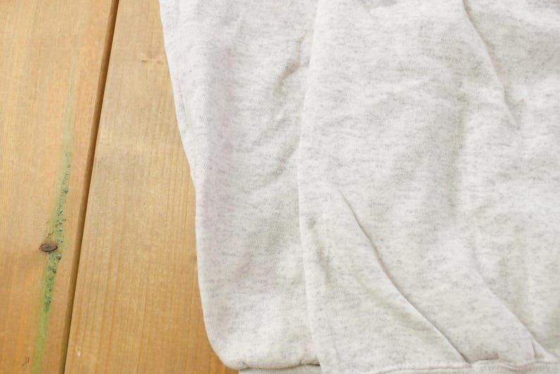 Op de afbeelding: Een lichtgrijs sweatshirt met een gespikkelde of gem&ecirc;leerde textuur door de hele stof. Het kledingstuk heeft een zacht, gevouwen uiterlijk met zichtbare kreukels en een consistent lichtgrijs kleurenpalet over het gehele oppervlak.