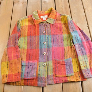 Peut inclure: Veste à carreaux multicolore avec une fermeture boutonnée et deux poches avant. La veste présente un mélange de couleurs vives, notamment le rouge, l'orange, le jaune, le bleu et le rose. La veste a un col et des manches longues. Les boutons sont de couleur claire avec un motif floral.