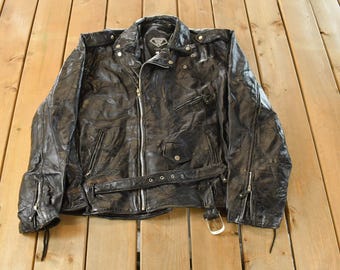 May include: A black leather jacket with a zip-up front, multiple pockets, and a belt. The jacket has a classic biker style with a notched collar and silver hardware. The leather appears worn, giving it a vintage look.