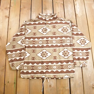 May include: A brown and white patterned fleece pullover with a mock neck and a button closure. The pullover has a drawstring at the bottom.
