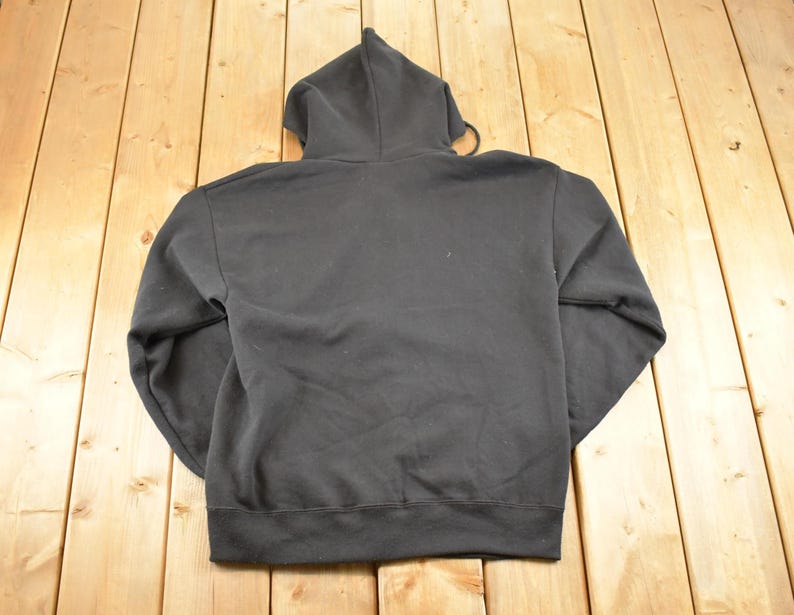 May include: A black hooded sweatshirt with a drawstring and a ribbed hem and cuffs. The back of the sweatshirt is visible, and it is made of a soft, comfortable material. The hoodie is a classic style.