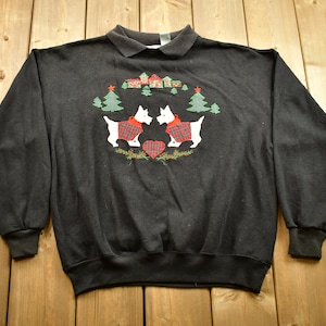 May include: Black sweatshirt with a Christmas-themed embroidered design featuring two white dogs wearing red and green plaid sweaters. The dogs are standing in front of a heart and two Christmas trees.