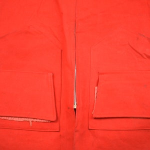 May include: A red jacket with two large pockets on the front. The jacket has a zipper down the front and is made of a thick, durable fabric.