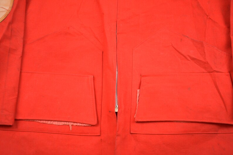 May include: A red jacket with two large pockets on the front. The jacket has a zipper down the front and is made of a thick, durable fabric.