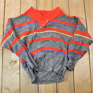 May include: A striped sweater with a red, gray, blue, yellow, and green color scheme. The sweater has a mock neck and a button closure.