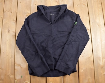May include: A dark blue long-sleeved shirt with a sailor collar and a small pocket on the right side. The shirt has a green patch on the right sleeve with two white stripes.