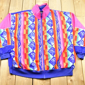 Könnte beinhalten: Eine bunte Jacke mit geometrischem Muster und Reißverschluss. Die Jacke ist aus leichtem Stoff und hat ein Farbschema in Pink, Blau, Rot, Grün und Gelb.