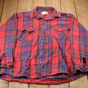 May include: Red, blue, and black plaid flannel shirt with long sleeves and two chest pockets.