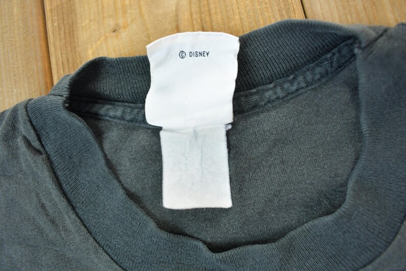 May include: A dark gray t-shirt with a white tag that says "&copy; DISNEY".