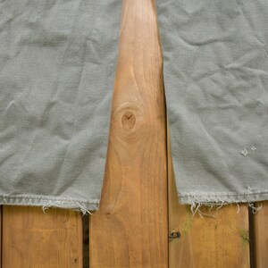 May include: A pair of grey cargo trousers with frayed hems. The trousers are laid flat on a wooden surface.