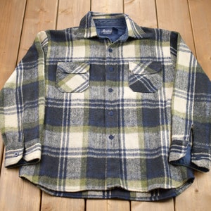 May include: A blue, green, and white plaid flannel shirt with long sleeves and two chest pockets.