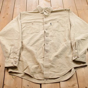 May include: A long-sleeved, light brown button-down shirt with two chest pockets and a single button cuff.