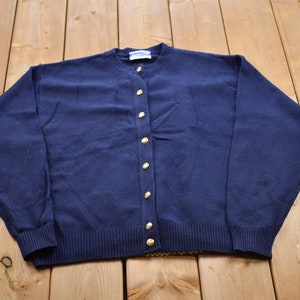 May include: A navy blue cardigan sweater with gold buttons. The sweater has long sleeves and a ribbed hem.