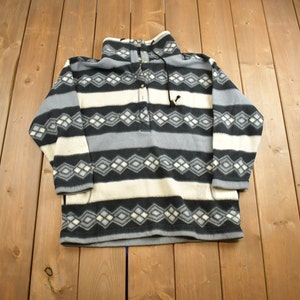 May include: A black, white, and gray striped fleece pullover with a diamond pattern. The pullover has a high neck and a button closure.