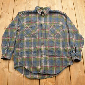 May include: A blue, green, and red plaid flannel shirt with long sleeves and two chest pockets.