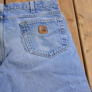 May include: A pair of light blue denim jeans with a back pocket featuring a brown Carhartt logo patch.