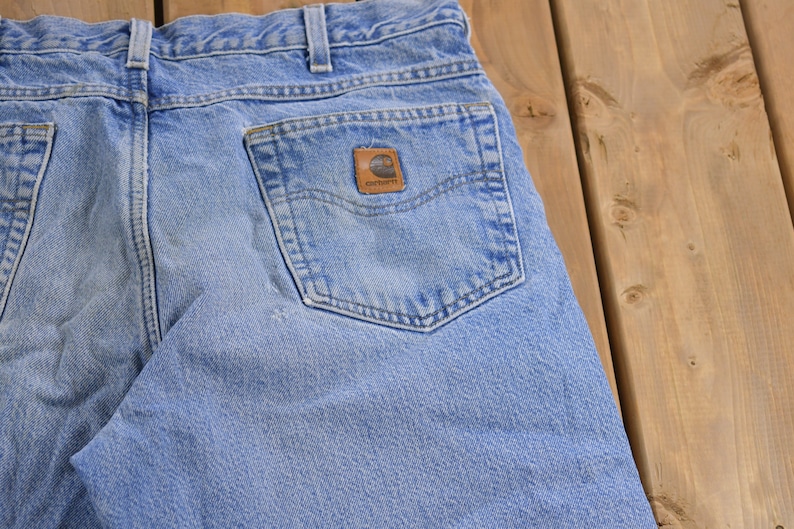May include: A pair of light blue denim jeans with a back pocket featuring a brown Carhartt logo patch.