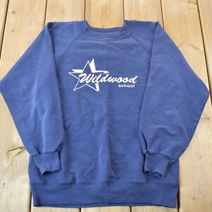 May include: A blue sweatshirt with a white star and the text "Wildwood School" printed on the front.