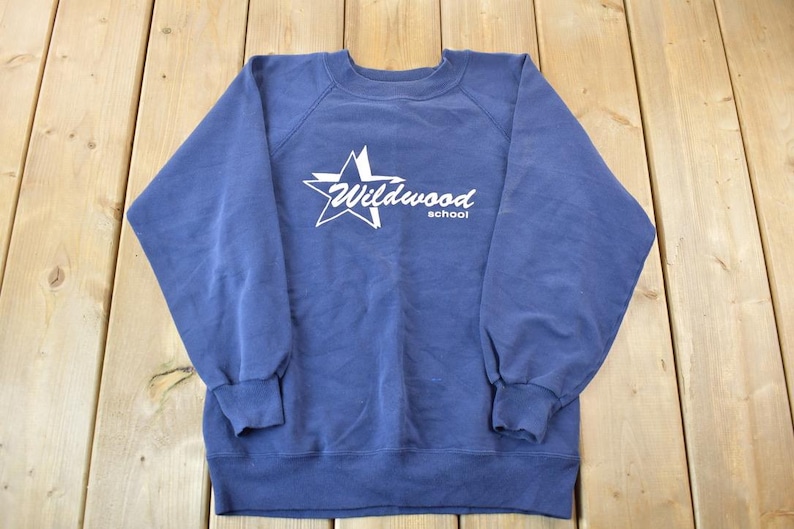 May include: A blue sweatshirt with a white star and the text "Wildwood School" printed on the front.