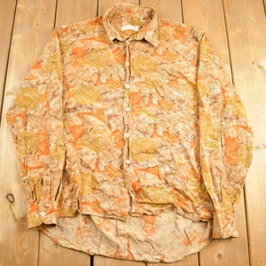 May include: A long-sleeved button-down shirt with a brown, orange and yellow camouflage print.