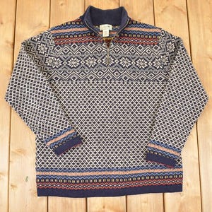 May include: A navy, cream, and red patterned sweater with a quarter-zip collar. The sweater features a geometric design with diamond and snowflake patterns. The cuffs and hem have a contrasting striped design.