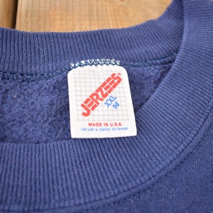 K&ouml;nnte beinhalten: Ein marineblauer Sweatshirt mit einem Jerzees-Etikett mit der Aufschrift "XXL 50" und "Made in U.S.A."