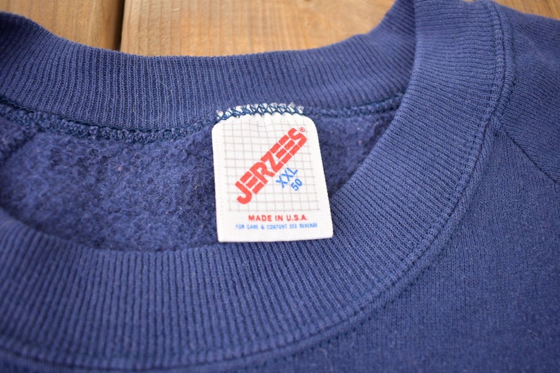 K&ouml;nnte beinhalten: Ein marineblauer Sweatshirt mit einem Jerzees-Etikett mit der Aufschrift "XXL 50" und "Made in U.S.A."