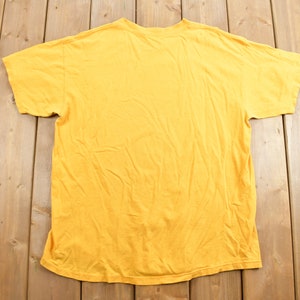 May include: A plain yellow t-shirt with short sleeves. The t-shirt is laid flat on a wooden surface.